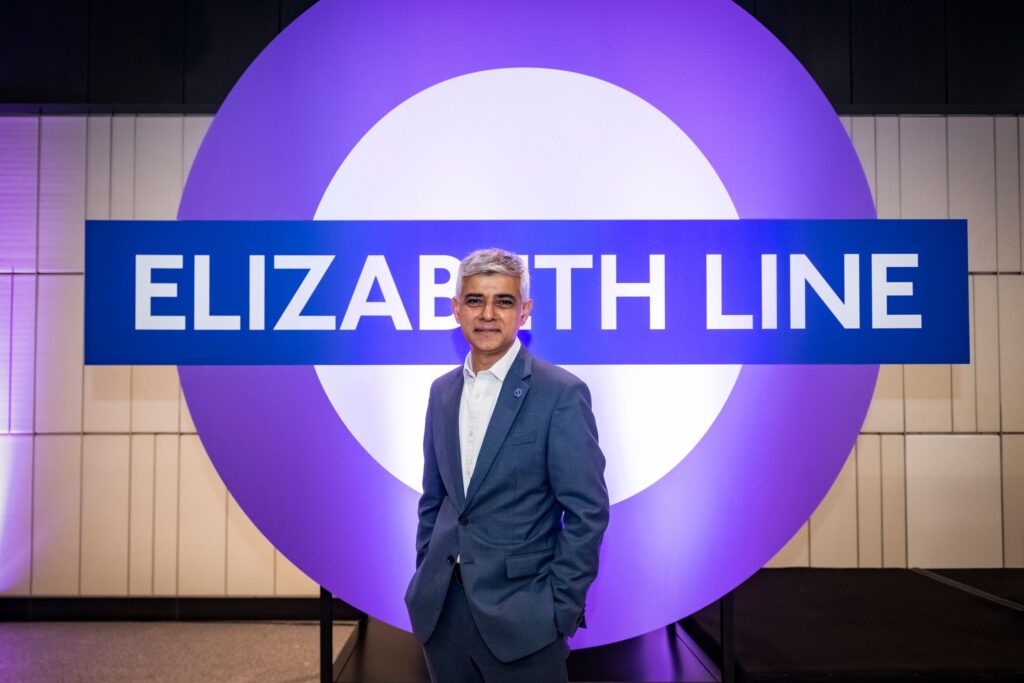 Sadiq Khan standing in front of a large purple Elizabeth line roundel