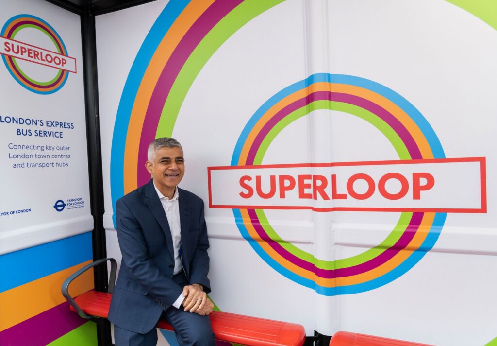 Sadiq sits at a bus stop wrapped with the colourful Superloop branding.