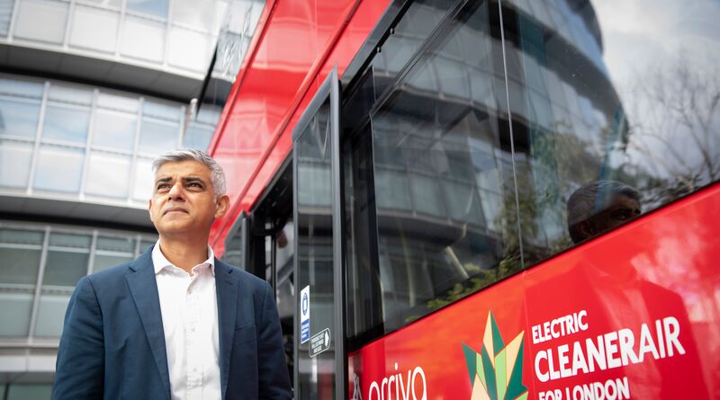 Sadiq stands next to a red bus with a logo that reads "Electric. Cleaner air for London."